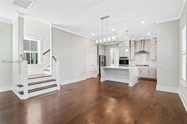 kitchen featuring pendant lighting, ornamental molding, a center island, stainless steel appliances, and wall chimney range hood