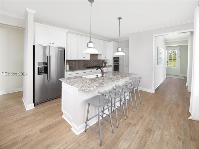 kitchen with sink, light stone counters, appliances with stainless steel finishes, a kitchen island with sink, and white cabinets