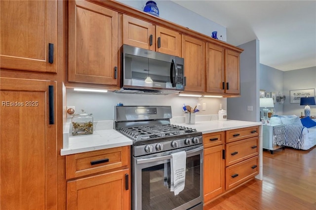 kitchen with stainless steel appliances, light stone counters, and light wood-type flooring