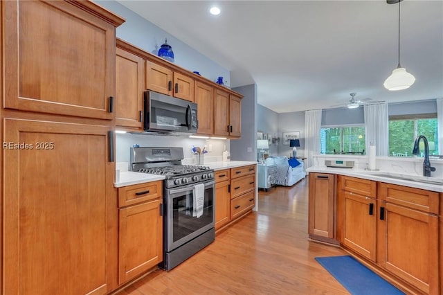 kitchen with sink, stainless steel gas range oven, decorative light fixtures, light wood-type flooring, and ceiling fan