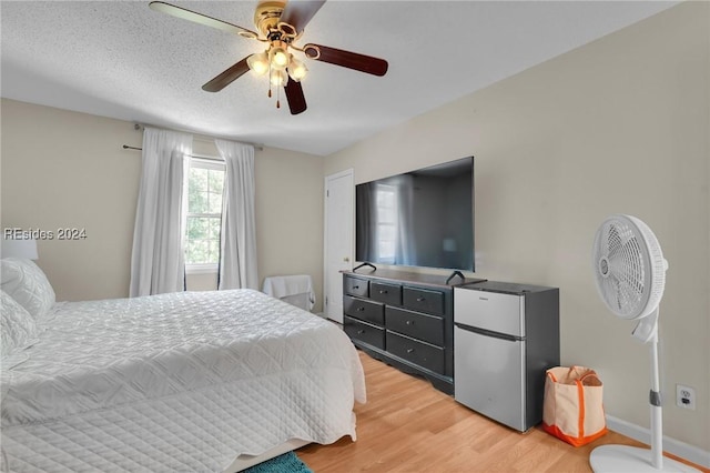 bedroom with a textured ceiling, stainless steel fridge, ceiling fan, and light hardwood / wood-style flooring