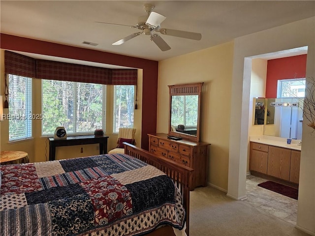 bedroom featuring light colored carpet, ceiling fan, and ensuite bath