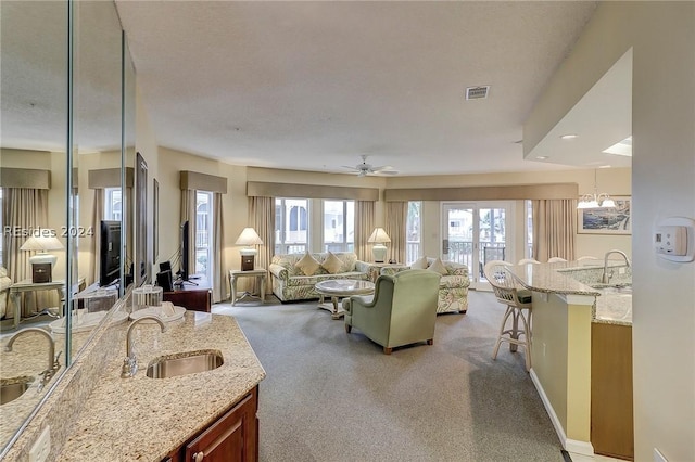 carpeted living room featuring sink, ceiling fan with notable chandelier, and a textured ceiling