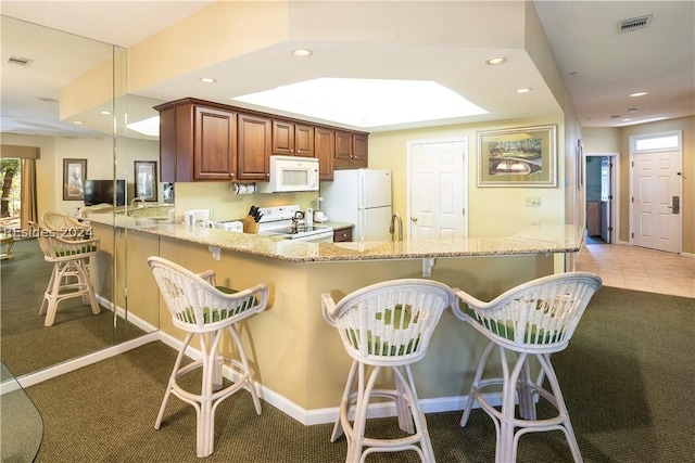 kitchen featuring light carpet, a kitchen breakfast bar, kitchen peninsula, white appliances, and light stone countertops