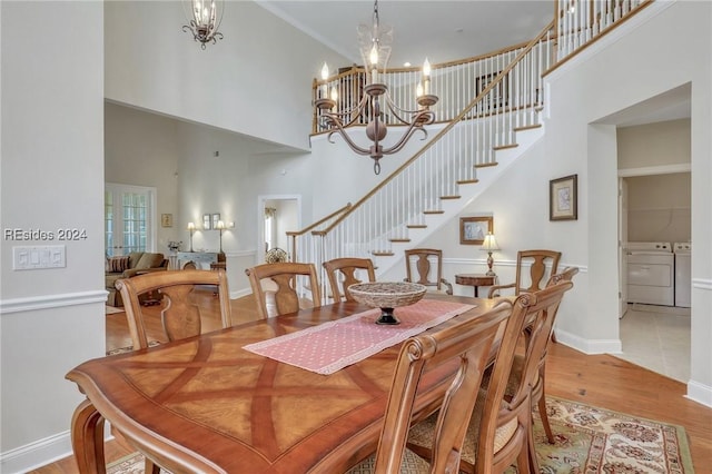 dining space featuring a towering ceiling, an inviting chandelier, washer and clothes dryer, and light wood-type flooring