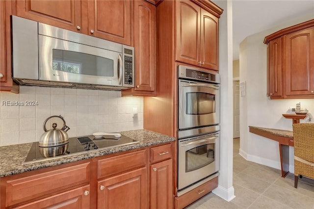 kitchen with tasteful backsplash, stainless steel appliances, light tile patterned floors, and dark stone countertops