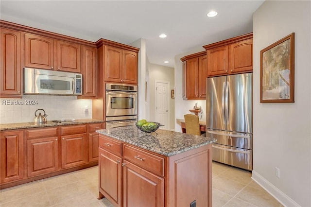 kitchen featuring light tile patterned floors, dark stone countertops, appliances with stainless steel finishes, a kitchen island, and backsplash