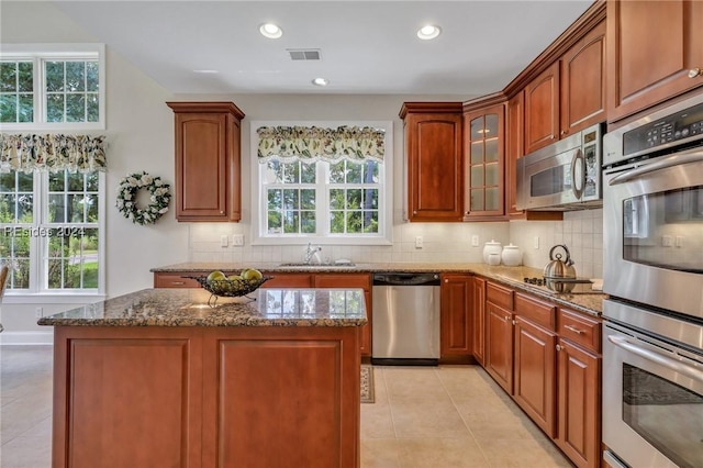 kitchen featuring stainless steel appliances, sink, dark stone countertops, a kitchen island, and a healthy amount of sunlight