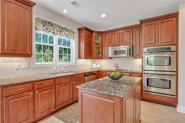 kitchen with light tile patterned flooring, a kitchen island, appliances with stainless steel finishes, sink, and light stone countertops