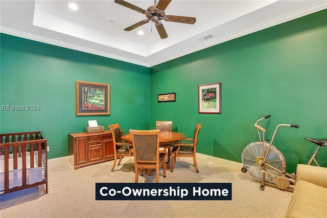 dining area featuring a tray ceiling, ornamental molding, light colored carpet, and ceiling fan