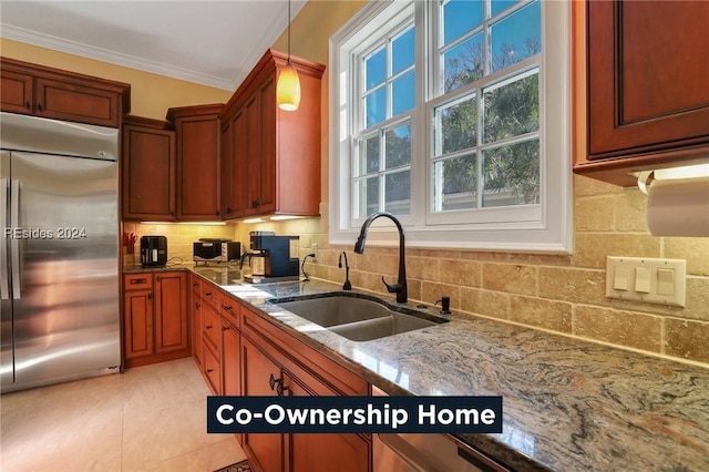 kitchen featuring sink, built in refrigerator, tasteful backsplash, stone countertops, and decorative light fixtures