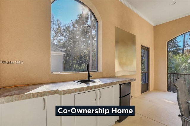 kitchen with white cabinetry, sink, tile counters, and crown molding