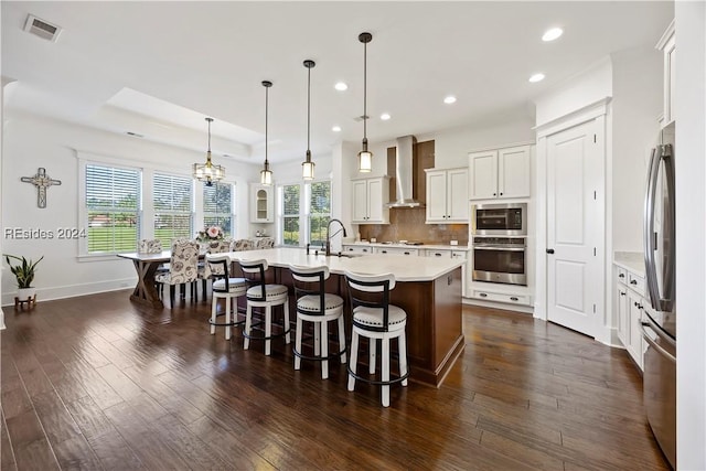 kitchen with decorative light fixtures, a large island with sink, a kitchen breakfast bar, wall chimney range hood, and backsplash