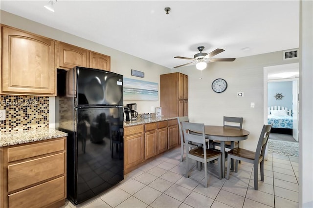 kitchen featuring ceiling fan, black refrigerator, light stone counters, tasteful backsplash, and light tile patterned flooring