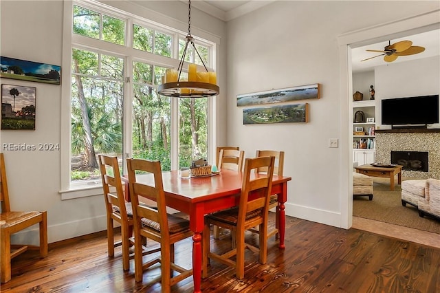 dining space with built in shelves, ornamental molding, dark hardwood / wood-style floors, ceiling fan, and a tiled fireplace