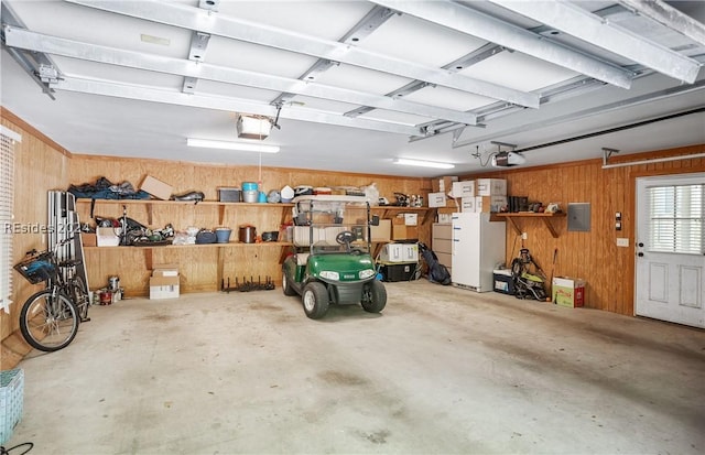 garage featuring white refrigerator, a garage door opener, electric panel, and wood walls