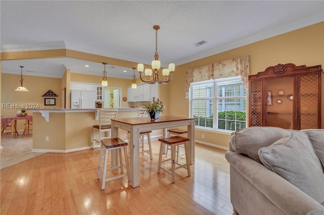 dining room with crown molding, light hardwood / wood-style floors, a textured ceiling, and a notable chandelier