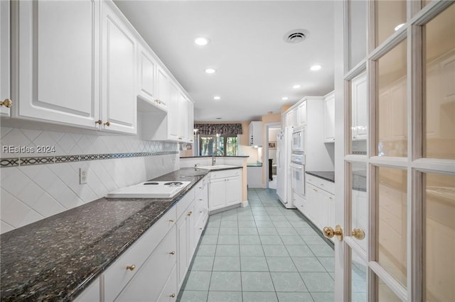 kitchen featuring white cabinetry, decorative backsplash, dark stone counters, light tile patterned floors, and white appliances