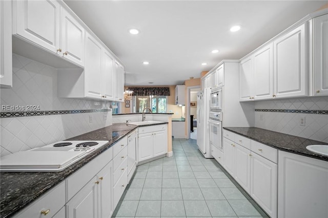 kitchen with sink, white cabinetry, dark stone countertops, light tile patterned floors, and white appliances