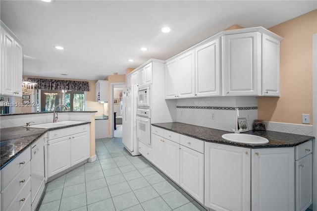 kitchen featuring white cabinetry, sink, dark stone countertops, kitchen peninsula, and white appliances