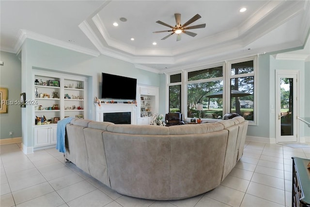 living room featuring built in shelves, crown molding, light tile patterned floors, a tray ceiling, and ceiling fan