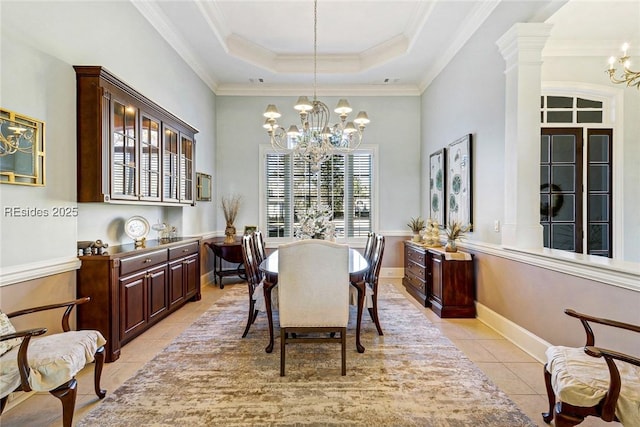 tiled dining space with a notable chandelier, a tray ceiling, ornamental molding, and ornate columns