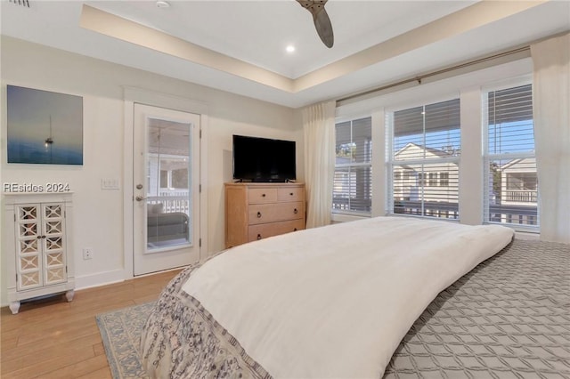 bedroom with access to outside, light hardwood / wood-style floors, a raised ceiling, and ceiling fan