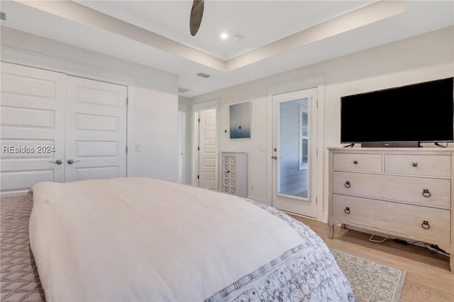 bedroom featuring ceiling fan, a tray ceiling, light hardwood / wood-style floors, access to outside, and a closet