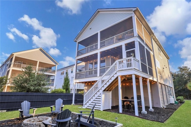 rear view of house with a sunroom, a lawn, and a fire pit