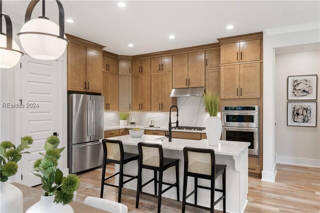 kitchen featuring a breakfast bar area, hanging light fixtures, appliances with stainless steel finishes, a kitchen island with sink, and light hardwood / wood-style floors