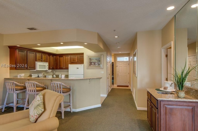 kitchen with a kitchen bar, kitchen peninsula, white appliances, and dark carpet