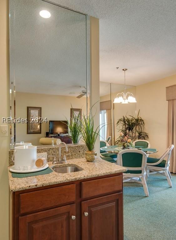 kitchen with sink, hanging light fixtures, carpet, light stone counters, and a textured ceiling