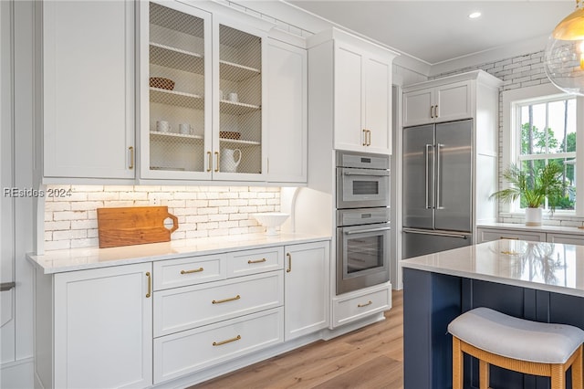 kitchen with tasteful backsplash, white cabinetry, appliances with stainless steel finishes, and light stone countertops