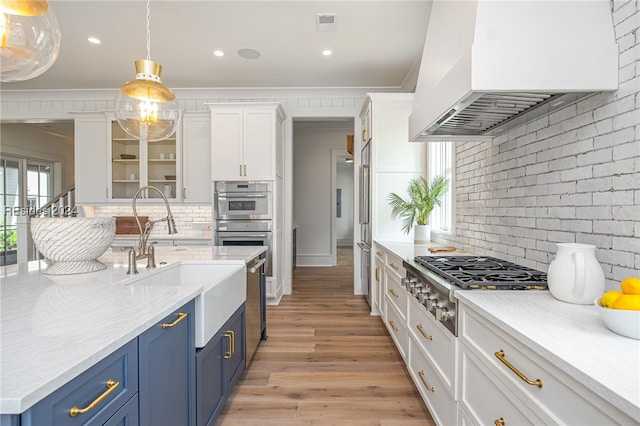 kitchen featuring premium range hood, stainless steel appliances, white cabinets, blue cabinets, and decorative light fixtures