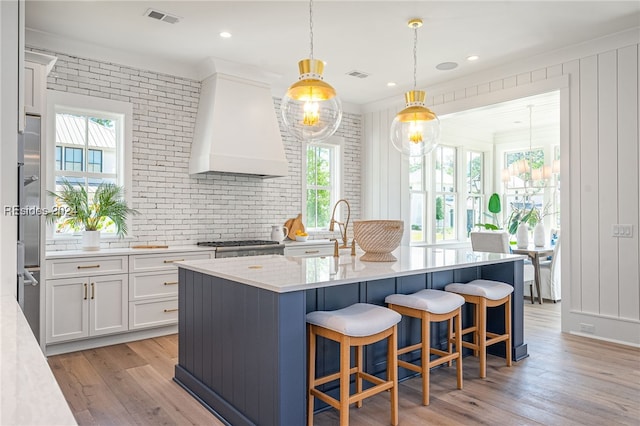 kitchen with pendant lighting, white cabinetry, an island with sink, sink, and custom exhaust hood