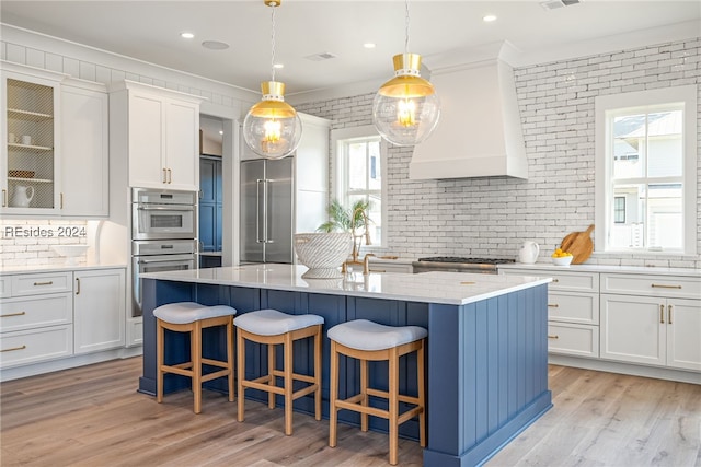 kitchen with pendant lighting, a kitchen breakfast bar, custom exhaust hood, a kitchen island with sink, and stainless steel appliances