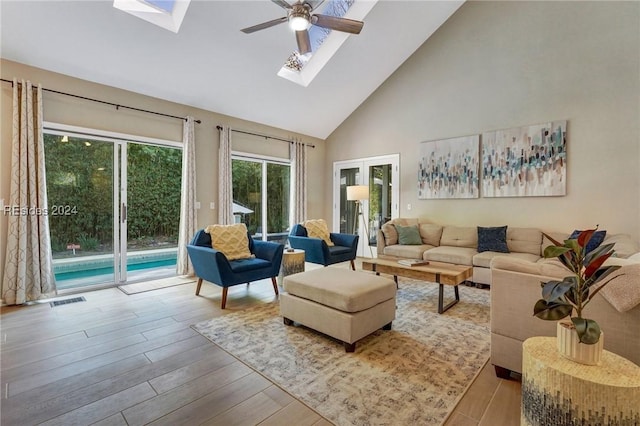 living room with light hardwood / wood-style flooring, a skylight, high vaulted ceiling, and ceiling fan