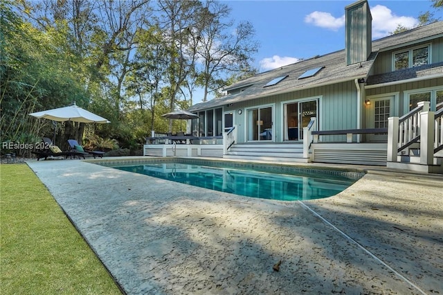 view of swimming pool with a wooden deck, a sunroom, and a patio area