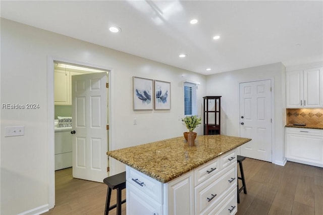 kitchen with white cabinetry, a kitchen breakfast bar, a center island, light stone counters, and dark wood-type flooring