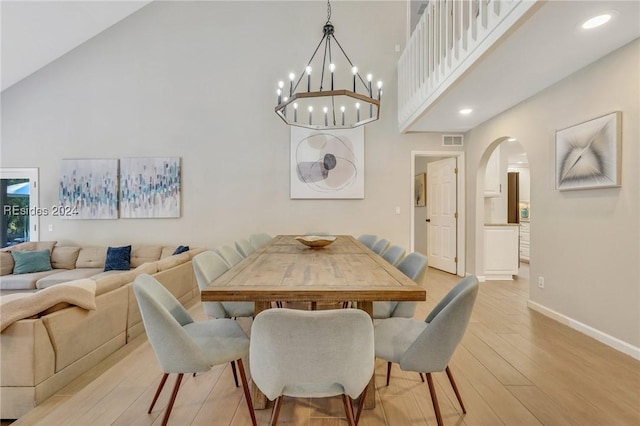 dining space with a towering ceiling, light hardwood / wood-style flooring, and a notable chandelier