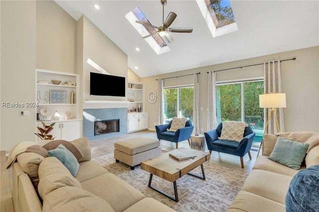 living room featuring ceiling fan, a skylight, high vaulted ceiling, a brick fireplace, and light wood-type flooring