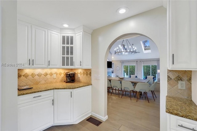 kitchen featuring white cabinetry, dark stone counters, light hardwood / wood-style flooring, and backsplash