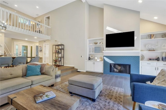 living room featuring wood-type flooring, a tiled fireplace, and high vaulted ceiling