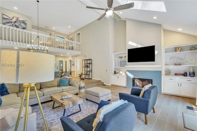 living room featuring high vaulted ceiling, light wood-type flooring, ceiling fan with notable chandelier, and a fireplace