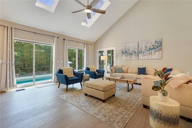 living room with ceiling fan, a skylight, high vaulted ceiling, and light hardwood / wood-style flooring