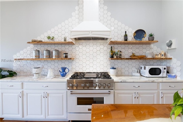 kitchen with tasteful backsplash, white cabinetry, high end stainless steel range, light stone countertops, and custom range hood