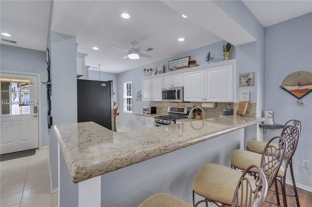 kitchen with appliances with stainless steel finishes, tasteful backsplash, white cabinetry, a breakfast bar area, and kitchen peninsula