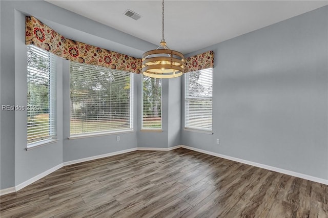 unfurnished dining area with an inviting chandelier and hardwood / wood-style flooring