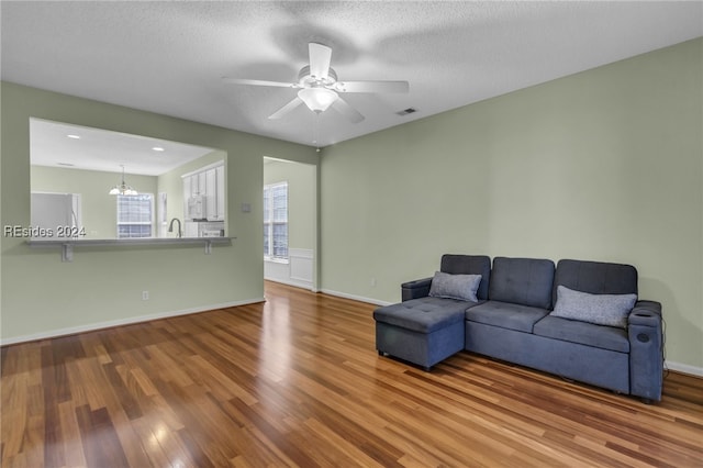 living room featuring wood-type flooring, sink, ceiling fan with notable chandelier, and a textured ceiling