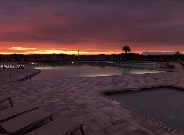 pool at dusk featuring a patio area and a water view